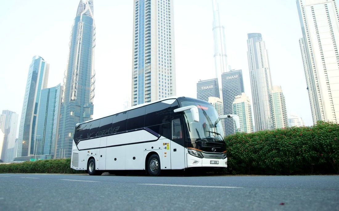 A white 50-seat coach on a Dubai road with the Downtown towers behind
