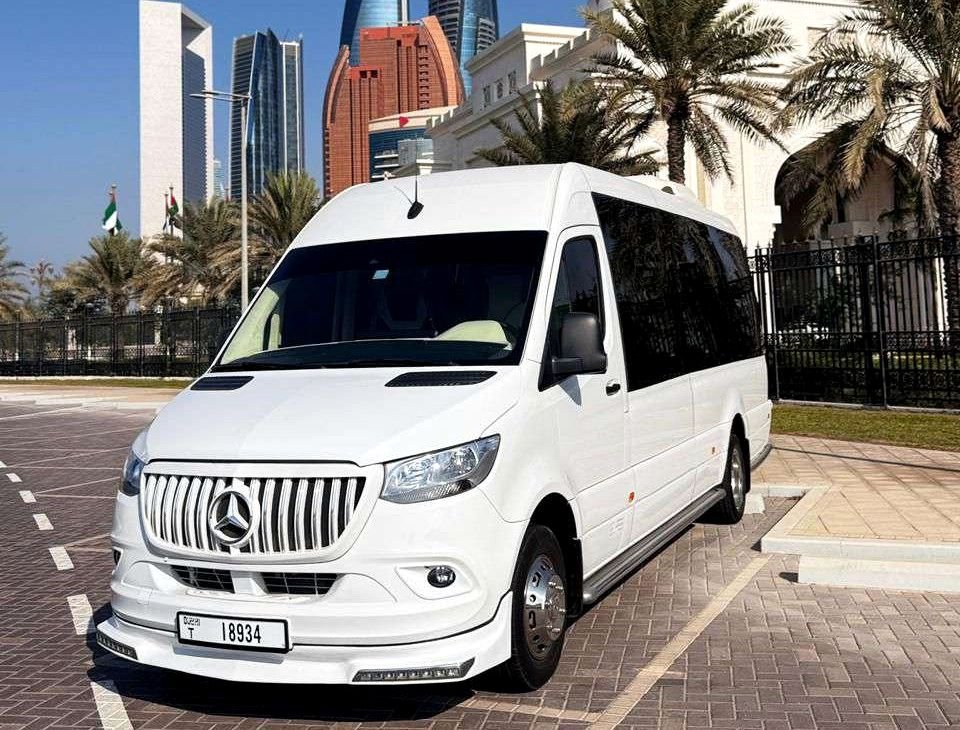 White Mercedes Sprinter minibus parked beside palm trees and city towers