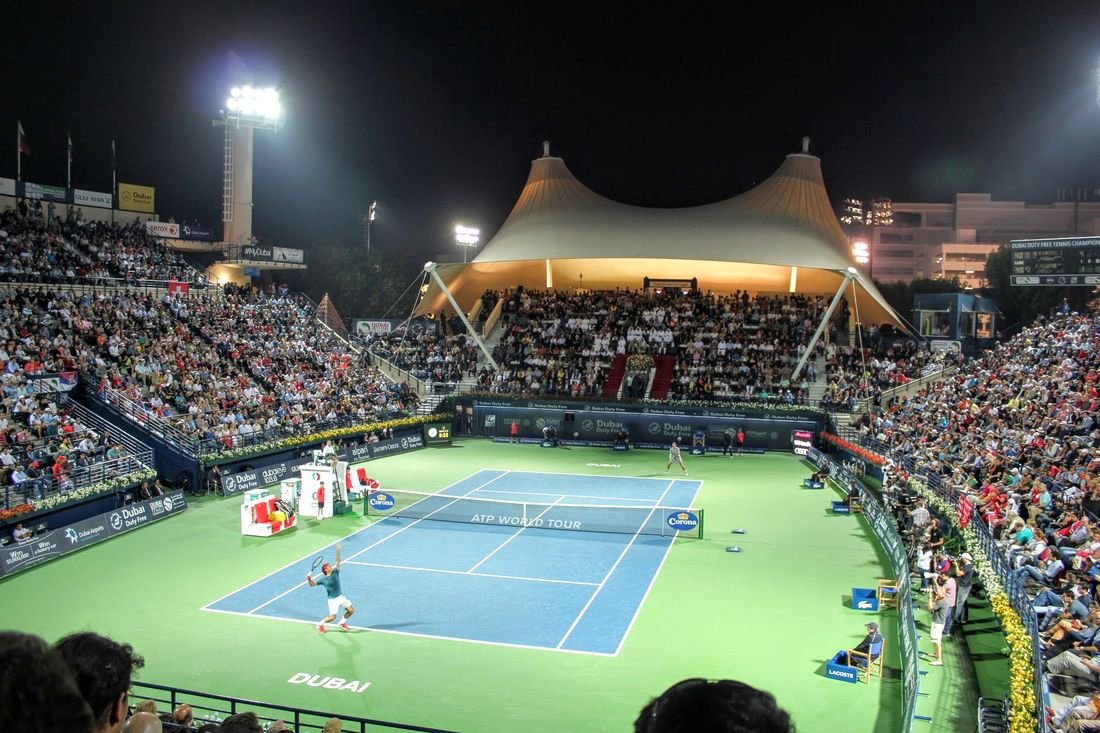 A floodlit tennis stadium in Dubai with a full crowd at night