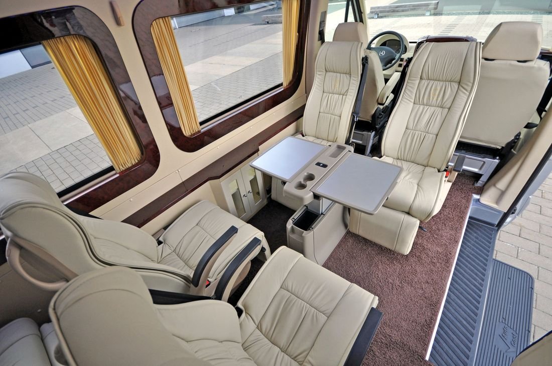 Cream leather captain’s chairs and fold-out tables inside a VIP Sprinter